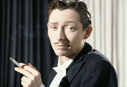 Tilda Swinton als man, ze kijkt met een sigaret in haar hand recht in de camera
