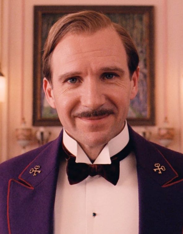 still uit The Grand Budapest Hotel, conciërge Gustave H kijkt recht in de camera
