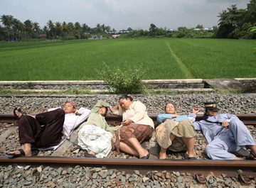 In een weelderig groen landschap liggen op de voorgrond vijf mensen duttend op het spoor