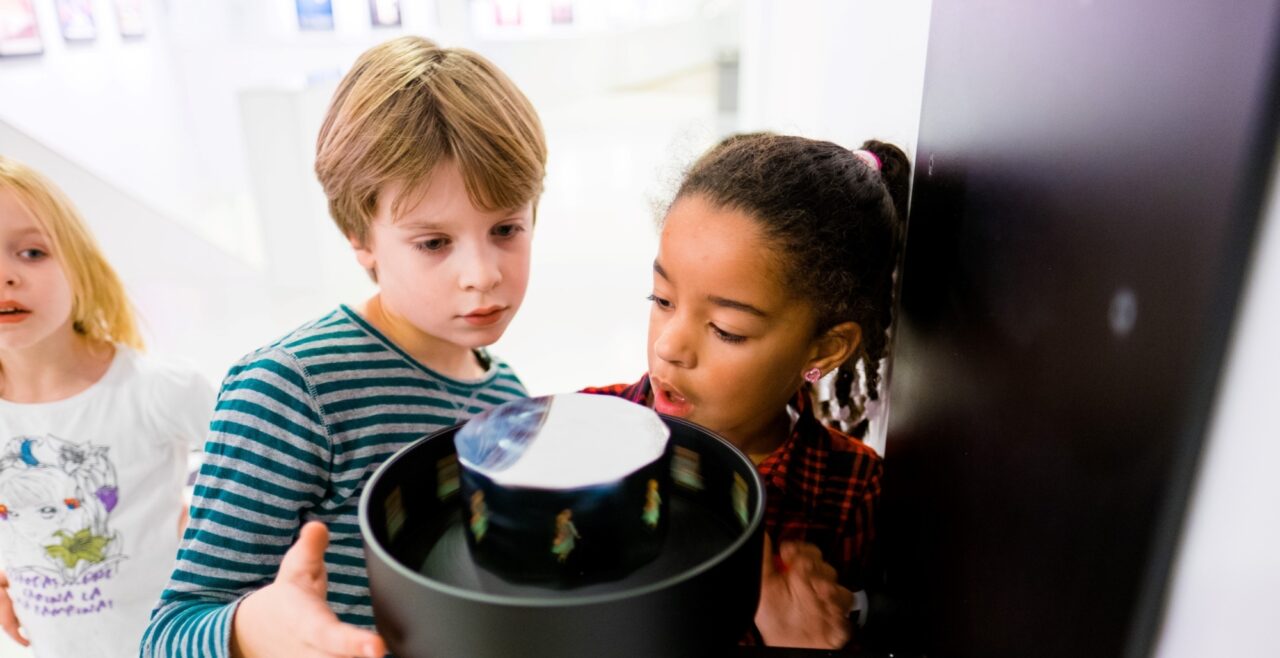 Drie kinderen bekijken een optische illusie die deel uitmaakt van de permanente tentoonstelling in Eye Filmmuseum