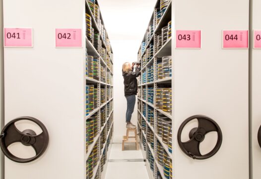 Een medewerker van Eye zet een stapel filmblikken in een grote archiefkast