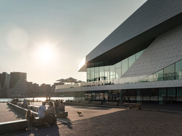 Mensen zitten op de kade voor Eye Filmmuseum met ondergaande zon