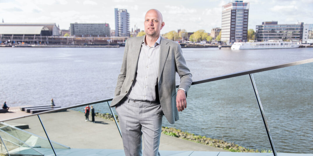 Wietse Potiek poseert op de houten trap die leidt naar de ingang van Eye Filmmuseum; op de achtergrond centraal station.