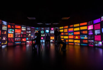 Volwassenen zitten en staan in het midden van een donkere ruimte, tegenover de muren bedekt met kleurrijke filmprojecties. De projecties zijn videofragmenten uit de Eye-collectie gesorteerd op kleur en thema